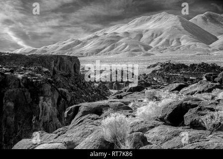 Rocky Felder, Felsen Schlucht mit steilen Felswände und karge Wüste Berge bei bewölktem Himmel. Infrarotbild, Schwarz und Weiß. Stockfoto