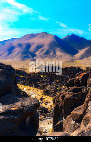 Auf der Suche durch felsige Schlucht, unfruchtbare Wüste Tal und die Berge unter strahlend blauen Himmel mit weißen Wolken. Stockfoto