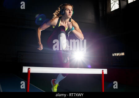 Junge Sportlerin laufen und springen über eine Hürde. Sprint Rennen mit Hürden leichtathletik Ausbildungskonzept Hintergrund Stockfoto