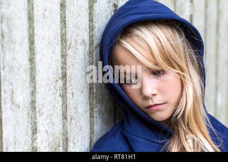 Portrait von traurigen blonde Mädchen trägt blaue Kapuzenjacke gegen Holz Wand lehnt Stockfoto