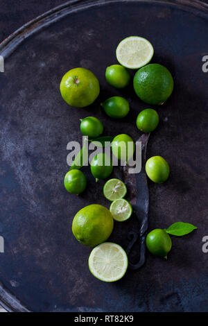 In Scheiben geschnitten und ganze limequats, Limes, Blätter und alten Messer auf dunklem Boden Stockfoto