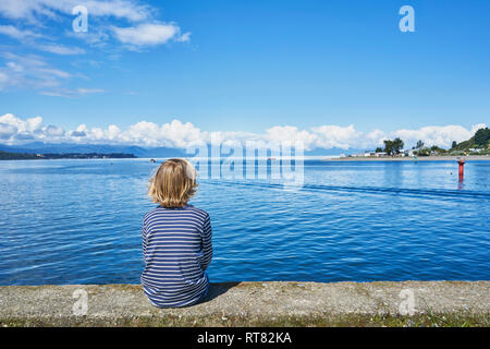 Chile, Puerto Montt, Junge sitzt auf der Kaimauer im Hafen Stockfoto