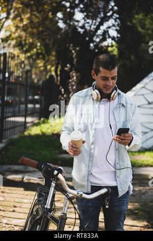 Junger Mann mit Fahrrad und Kaffee zum Mitnehmen Handy prüfen. Stockfoto