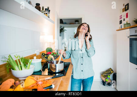 Lachende Frau am Telefon zu sprechen, während der Vorbereitung Kürbissuppe Stockfoto