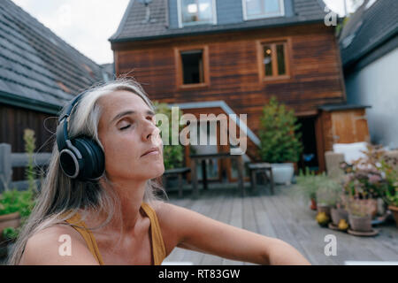 Portrait von reife Frau Musik hören mit Kopfhörern auf der Terrasse Stockfoto