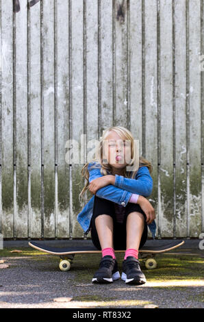 Portrait von Mädchen auf Skateboard vor der hölzernen Wand heraus haften Zunge Stockfoto