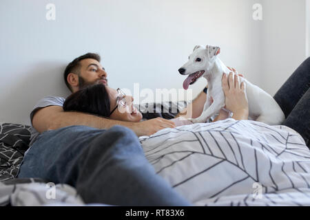 Paar liegend auf Bett kuscheln Hund Stockfoto