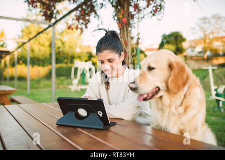 Lächelnde junge Frau mit einem Tablet in einem Park mit ihrem Hund Stockfoto