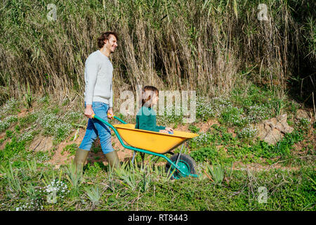 Vater gehen auf einem Feldweg, Schubkarre, mit seinem Sohn sitzen Stockfoto