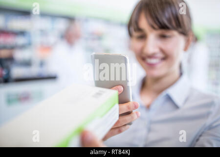 Lächelnde Frau in der Apotheke holding Smartphone und Medizin Stockfoto