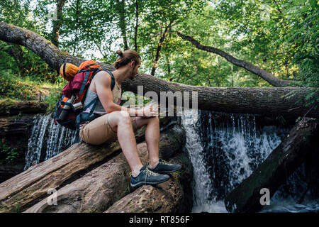 Junger Mann mit Rucksack in eine Pause in einem Wald in der Nähe von Wasserfall Stockfoto