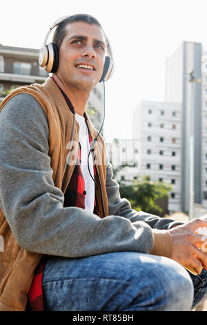 Lächelnden jungen Mann sitzt im Freien in der Stadt Kopfhörer tragen Stockfoto