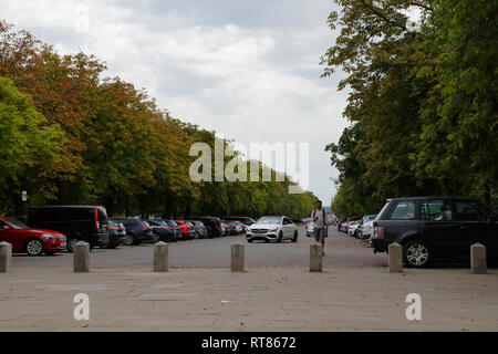 Ein Mann Spaziergänge entlang wie Autos kommen auf einem Parkplatz zu parken (Parkplatz) in Greenwich in London, Vereinigtes Königreich. Stockfoto