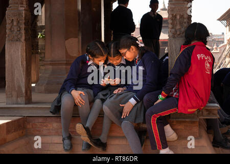 Nepal, Kathmandu Tal, Bhaktapur, Durbar Square, Schülerinnen sitzen im Schatten der Chyasilin Mandap am Bildschirm des Smartphones auf der Suche Stockfoto