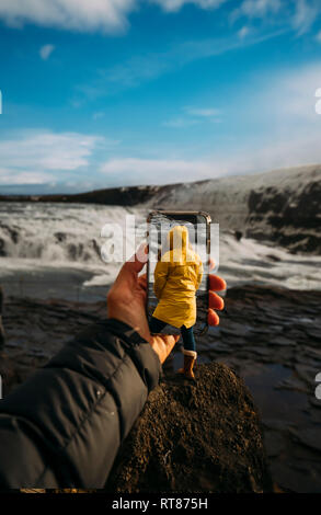 3D-Montage der Mann unter Smartphone Bild der isländischen Landschaft und Frau tragen gelbe Regenmantel Stockfoto