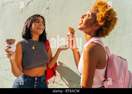 Zwei glückliche weibliche Freunde mit Eistüten an einer Wand Stockfoto