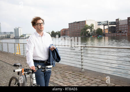 Deutschland, Berlin, Porträt der Geschäftsmann mit Smartphone und Kopfhörer, während sein Rad schieben Stockfoto