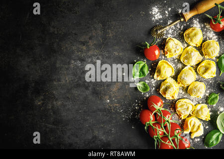 Essen Hintergrund. Italienisches Essen Hintergrund mit Ravioli, Tomaten, Oliven und Basilikum auf dunklem Hintergrund. Horizontal mit kopieren. Stockfoto