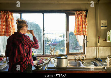 Frau, die in der Küche vorbereiten Essen und Trinken aus dem Becher Stockfoto