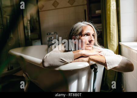 Portrait von traurige Frau in der Badewanne gekleidet sitzen Stockfoto