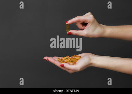 Die Streuung der transparent gelb Pillen. Handvoll Kapseln in der Handfläche, Nahaufnahme, auf grauem Hintergrund. Kapseln Fischöl, Omega 3. Gesundheit Stockfoto