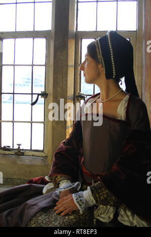 Eine schöne junge Frau gekleidet, wie Anne Boleyn durch ein Fenster im Tower von London sitzt und sieht nachdenklich aus. Stockfoto