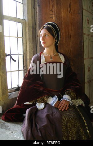 Eine schöne junge Frau gekleidet, wie Anne Boleyn durch ein Fenster im Tower von London sitzt und sieht nachdenklich aus. Stockfoto