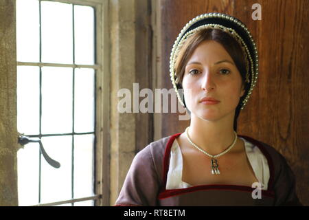 Eine schöne junge Frau gekleidet, wie Anne Boleyn durch ein Fenster im Tower von London sitzt und sieht nachdenklich aus. Stockfoto