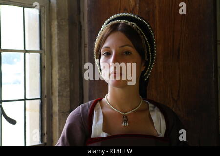 Eine schöne junge Frau gekleidet, wie Anne Boleyn durch ein Fenster im Tower von London sitzt und sieht nachdenklich aus. Stockfoto