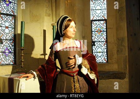 Eine schöne junge Frau gekleidet, wie Anne Boleyn durch ein Fenster im Tower von London sitzt und sieht nachdenklich aus. Stockfoto