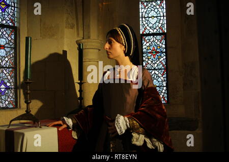 Eine schöne junge Frau gekleidet, wie Anne Boleyn durch ein Fenster im Tower von London sitzt und sieht nachdenklich aus. Stockfoto