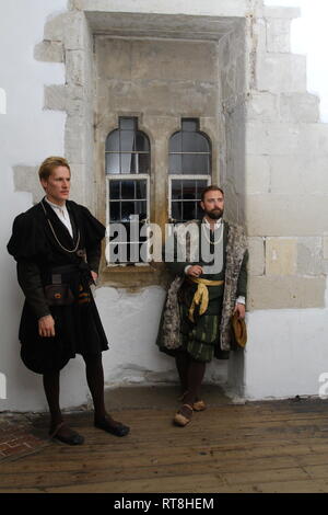 Zwei Tudor Männer tragen Regal Wäscheständer durch Glasfenster in einem alten Haus - sie tragen authentische historische Kleid Stockfoto