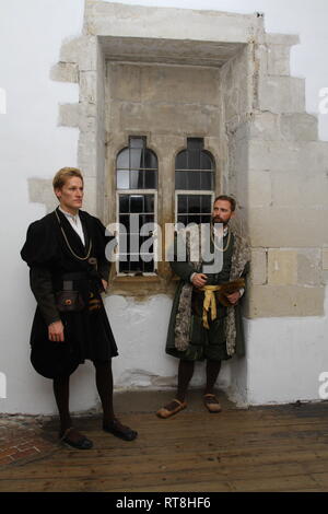 Zwei Tudor Männer tragen Regal Wäscheständer durch Glasfenster in einem alten Haus - sie tragen authentische historische Kleid Stockfoto