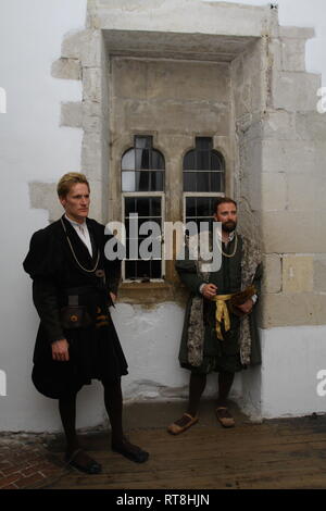 Zwei Tudor Männer tragen Regal Wäscheständer durch Glasfenster in einem alten Haus - sie tragen authentische historische Kleid Stockfoto