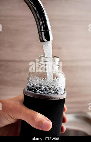 Nahaufnahme von einem jungen Mann cacausian füllen Sie ein Glas wiederverwendbare Trinkflasche mit Wasser aus einem Hahn ein gefiltertes Wasser Station oder eine häusliche Küche Stockfoto