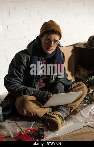 Ernsthafte Obdachloser in Gläsern mit Laptop Stockfoto