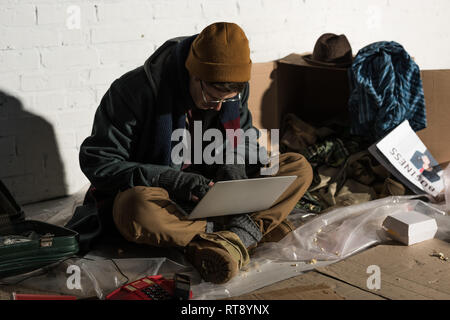 Obdachloser in Gläsern und fingerlose Handschuhe mit Laptop Stockfoto