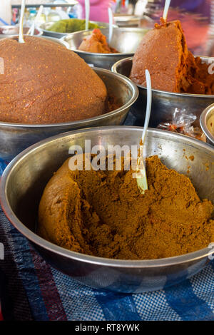 In der Nähe der bunten Schüsseln mit frisch zubereiteten Curry Paste für Verkauf bei Thai Food Market, mit Löffel in jede Schüssel, Braun und Rot sind die Farben Stockfoto