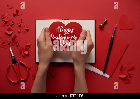 7/8-Ansicht von Frau mit Papier schneiden Herz Zeichen mit "Happy Valentines Day" Schrift auf rotem Hintergrund Stockfoto