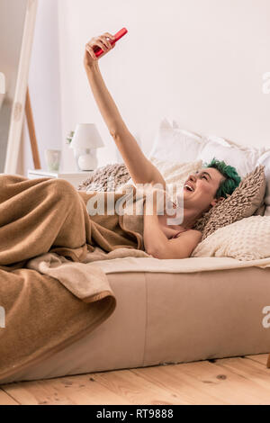 Lustig positive Frau, video chat, während im Bett lag, Stockfoto