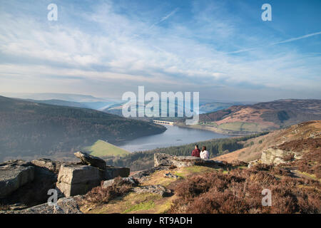 Junges Paar saß auf Bamford Kante im Peak District mit Blick über die Landschaft in der Ferne Ladybower Reservoir an einem Wintertag Stockfoto