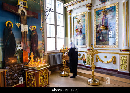 Lettland: Riga. St. Alexander Nevsky Kirche, neo-klassischen Stil, in der Straße, mit einer Frau das Tragen eines Fichu auf ihrem Kopf eine Kerze anzünden. Die Hälfte o Stockfoto