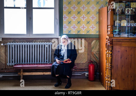 Lettland: Riga. Im neo-klassischen Stil St. Alexander Nevsky Kirche, in der Straße, eine Frau bekleidet Fichu auf dem Kopf lesen ein Gebet Boo Stockfoto