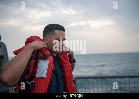 U.S. Navy Seaman Pedro Sanchez, aus Sacramento, Kalifornien, zieht eine Schwimmweste auf dem Flugdeck der geführten Anti-raketen-Zerstörer USS Stockdale (DDG106) für kleine Boot in den Arabischen Golf, Jan. 29, 2019 vorzubereiten. Die Stockdale ist in die USA 5 Flotte Bereich der Maßnahmen zur Unterstützung der Marine im Einsatz für die Stabilität und Sicherheit in der Region zu gewährleisten und verbindet das Mittelmeer und den Pazifischen Raum durch den westlichen Indischen Ozean und drei strategischen Punkten ersticken. Stockfoto