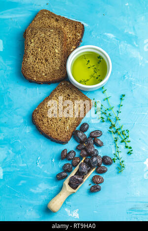 Traditionelle griechische italienische Vorspeisen getrocknete schwarze Oliven mit Brot und Olivenöl auf über einem blauen Beton Tischfläche Hintergrund serviert. Stockfoto