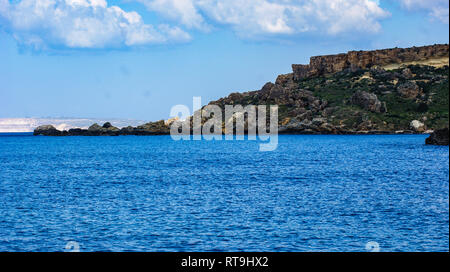 Das Mittelmeer Bucht von Gneina Bucht auf der Insel Malta. Der Strand und die Insel Gozo im entfernten Hintergrund vor blauem Himmel. Stockfoto