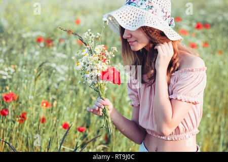 Beautieful junge Mädchen im Bereich der wilden Blumen. Jugendmädchen Ernte der Blumen auf der Wiese, holding Blumenstrauß. Sie trägt Hut Stockfoto