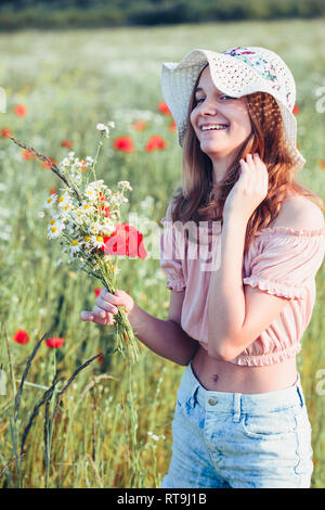 Beautieful junge Mädchen im Bereich der wilden Blumen. Jugendmädchen Ernte der Blumen auf der Wiese, holding Blumenstrauß. Sie trägt Hut Stockfoto