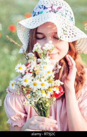 Beautieful junge Mädchen im Bereich der wilden Blumen. Jugendmädchen Ernte der Blumen auf der Wiese, holding Blumenstrauß. Sie trägt Hut Stockfoto