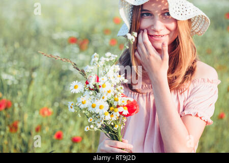 Beautieful junge Mädchen im Bereich der wilden Blumen. Jugendmädchen Ernte der Blumen auf der Wiese, holding Blumenstrauß. Sie trägt Hut Stockfoto